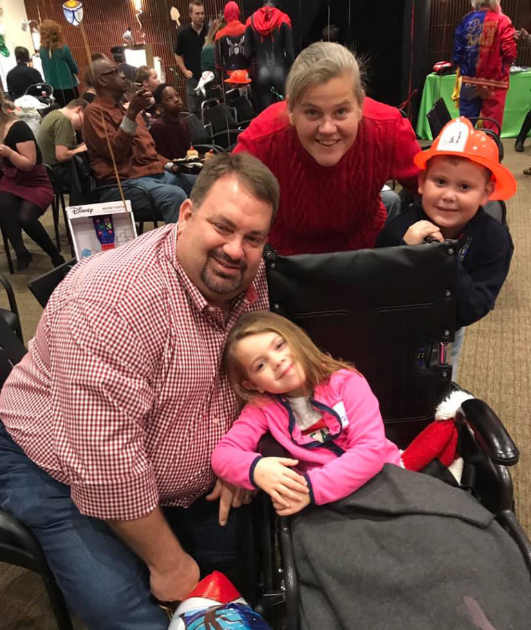 Couple with a young girl in a wheelchair and a young boy with an orange plastic firefighter hat