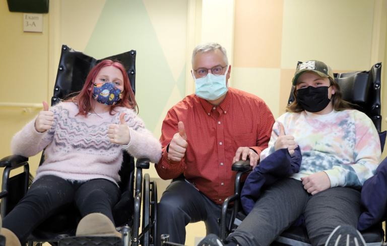 Dr. Standard between two girl patients in wheelchairs all giving the thumbs up sign.