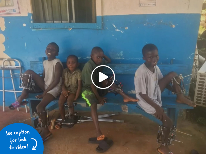 Four boys wearing external fixators sitting on a bench outside a hospital in Liberia