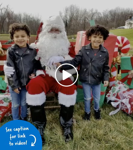 A young patient and his twin brother standing on either side of Santa Claus on a farm