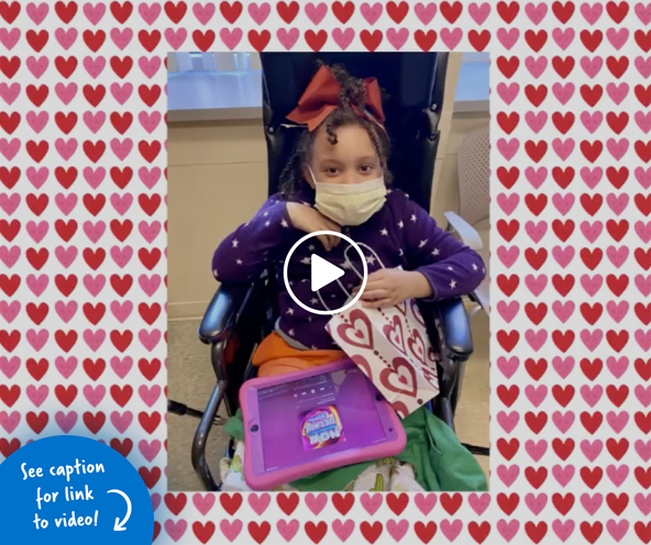 Young girl sitting in a wheelchair holding a goody bag covered in hearts