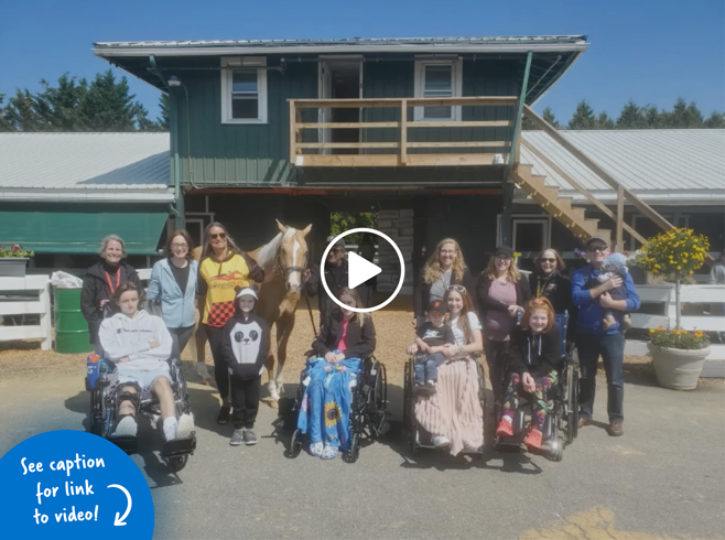 Photo of four children in wheelchairs and their families standing with Pediatric Liaison Marilyn Richardson and a horse and Pimlico staff infront of a stable house at Pimlico Race Track