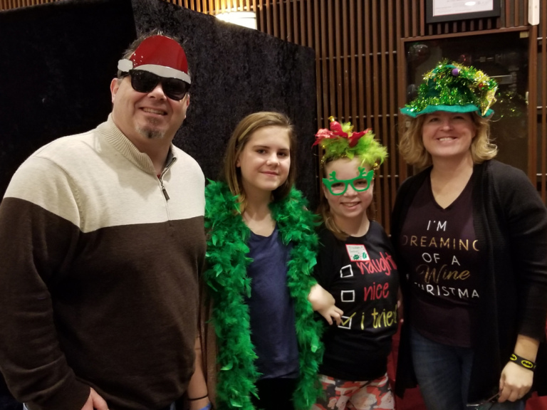 Parents with 2 children dressed in fun holiday-themed photo booth accessories at the International Center for Limb Lengthening pediatric holiday party