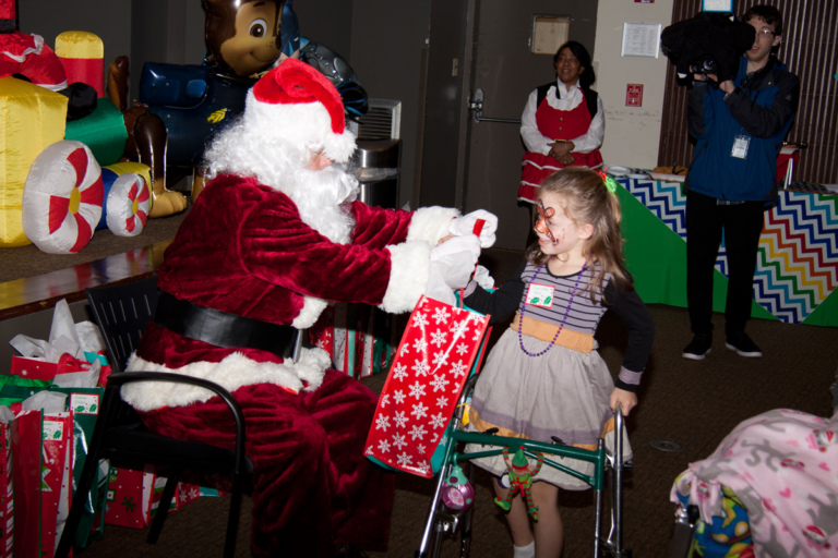 Santa gives present to girl patient with a walker at the International Center for Limb Lengthening pediatric holiday party