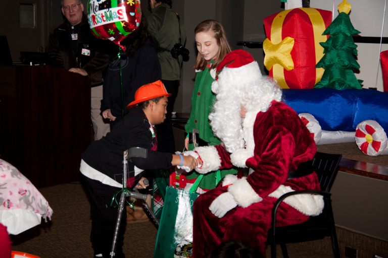 Santa shaking hands with patient on forearm crutches at the International Center for Limb Lengthening pediatric holiday party