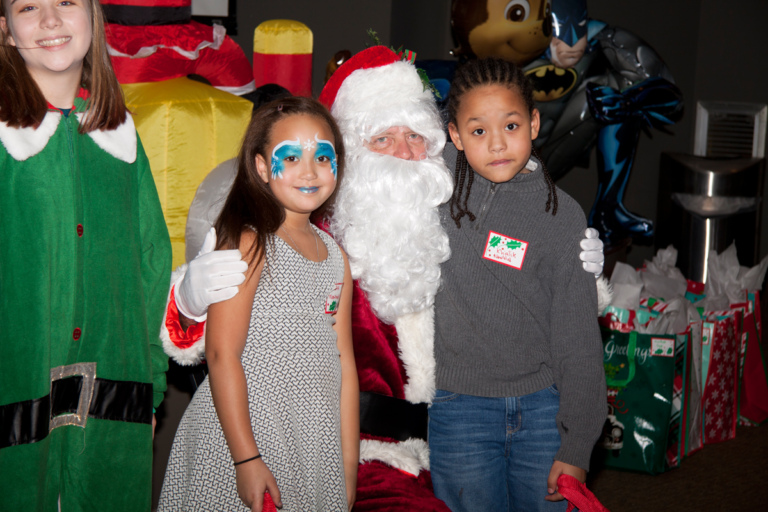 Santa and elf pose for picture with 2 children, one wearing face makeup, at the International Center for Limb Lengthening pediatric holiday party