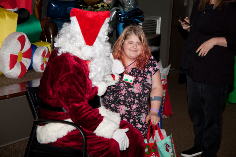 Santa talks with girl with forearm crutches and present at the International Center for Limb Lengthening pediatric holiday party