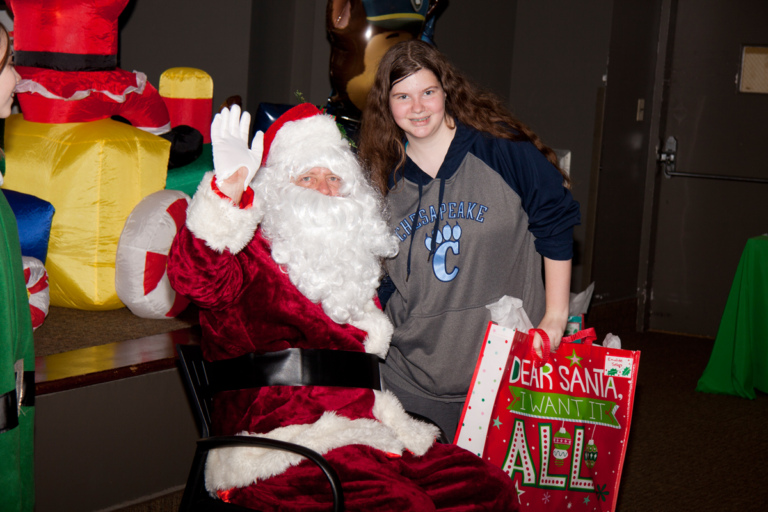 Santa waves and poses with girl with present at the International Center for Limb Lengthening pediatric holiday party