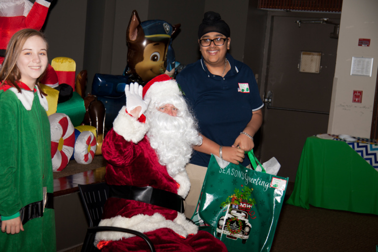 Santa waves and poses with boy with present at the International Center for Limb Lengthening pediatric holiday party