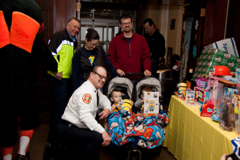 Fireman giving twin boys in strollers Minions toys at the International Center for Limb Lengthening pediatric holiday party