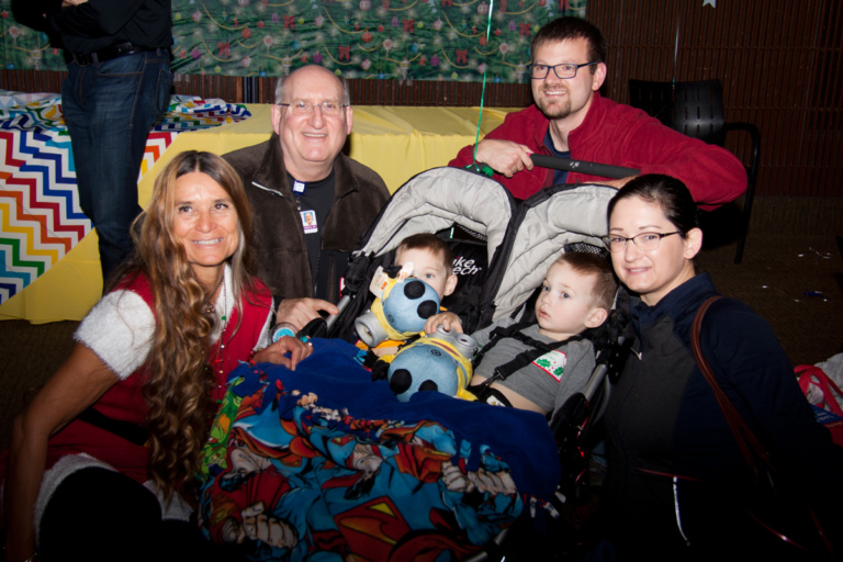 Dr. John Herzenberg and Marilyn Richardson, Pediatric Liaison, with a family with twin boys in strollers at the International Center for Limb Lengthening pediatric holiday party