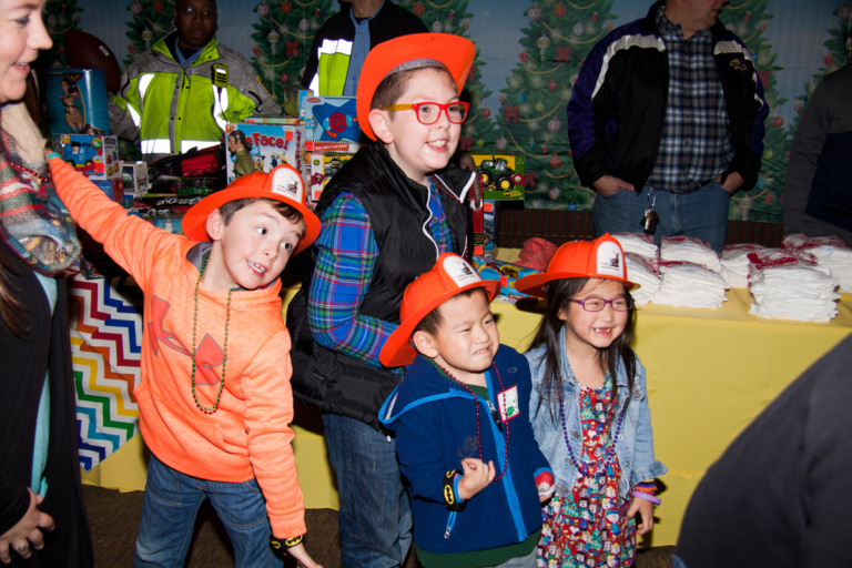 4 young kids smiling wearing toy orange firefighter hats at the International Center for Limb Lengthening pediatric holiday party