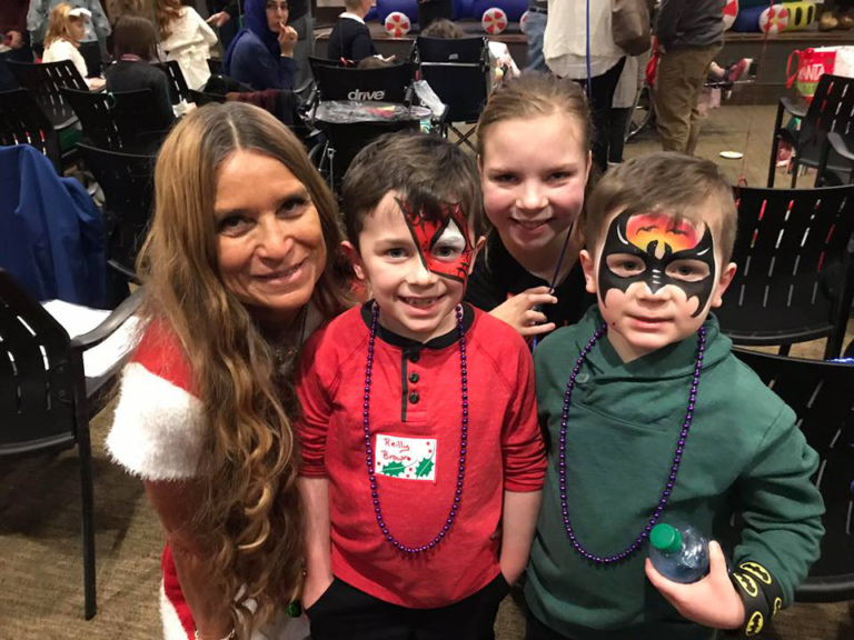 Marilyn Richardson, Pediatric Liaison, with one girl and two boys wearing superhero face paint at the International Center for Limb Lengthening pediatric holiday party