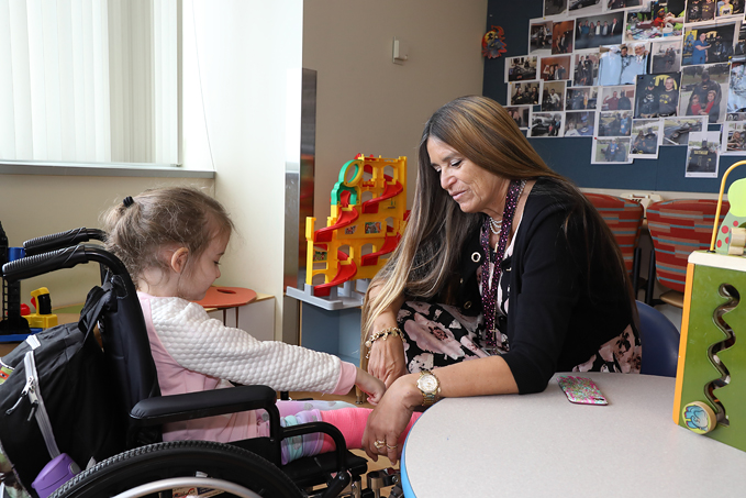 International Center for Limb Lengthening Child Life Specialist Marilyn Richardson comforting a young girl in a wheelchair in clinic waiting area