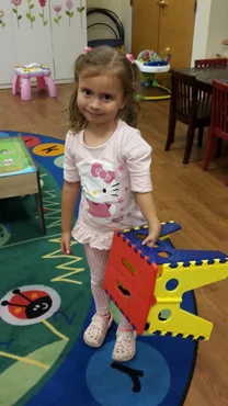 Anicka using her treated hand to hold up a play stool in a play room