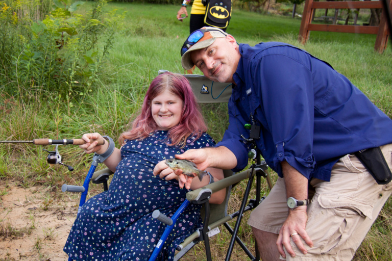 Dr. Shawn Standard poses with girl with forearm crutches showing caught fish at Rubin Institute for Advanced Orthopedics 2018 Save-A-Limb Pool Party event