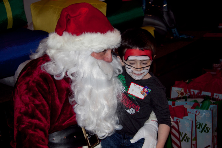 Young boy with Santa face painting sits on Santa’s lap at the International Center for Limb Lengthening pediatric holiday party