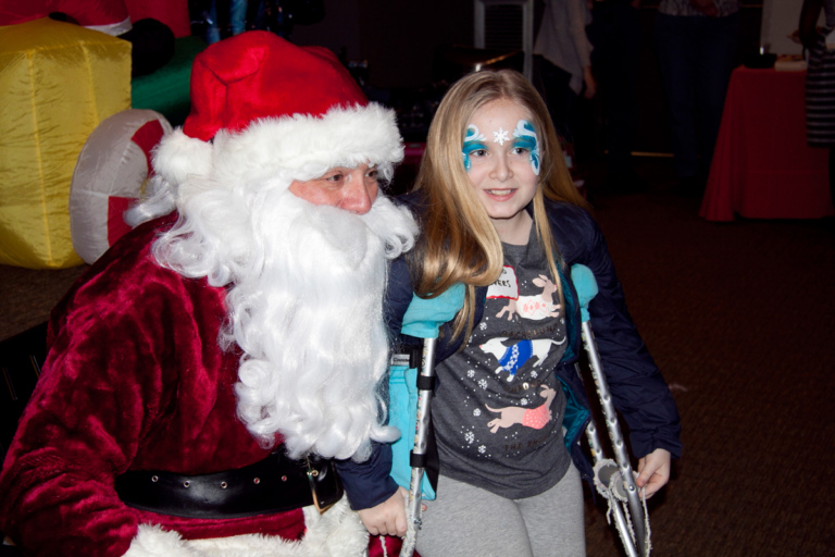 Young girl with crutches and face paint takes picture with Santa at the International Center for Limb Lengthening pediatric holiday party