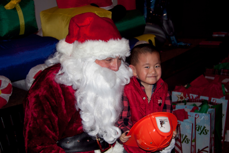 Young boy with fireman hat sits on Santa’s lap at the International Center for Limb Lengthening pediatric holiday party