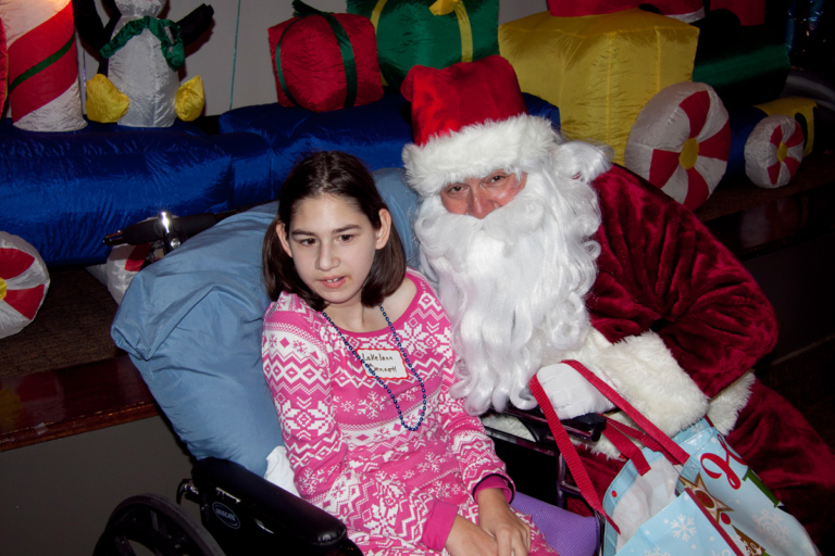 Girl in wheelchair takes a picture with Santa at the International Center for Limb Lengthening pediatric holiday party