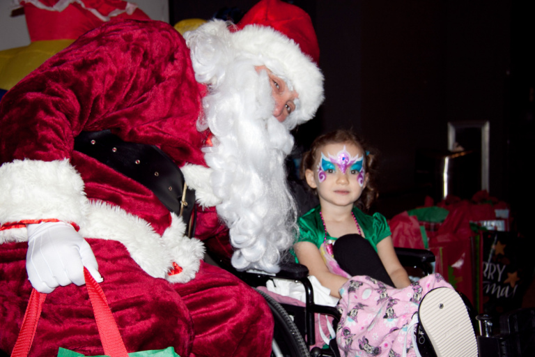 Young girl in a wheelchair with face painted has picture taken with Santa at the International Center for Limb Lengthening pediatric holiday party