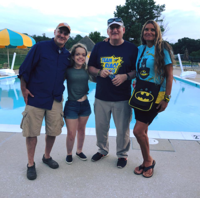 Dr. Shawn Standard, Dr. John Herzenberg, Pediatric Liaison Marilyn Richardson and female patient pose in front of pool at Rubin Institute for Advanced Orthopedics 2018 Save-A-Limb Pool Party event