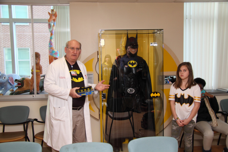 Dr. John Herzenberg speaks in front of Leonard B. “Batman” Robinson’s Batman suit in glass case at the International Center for Limb Lengthening’s Leonard B. “Batman” Robinson Memorial Valentine’s Day Party