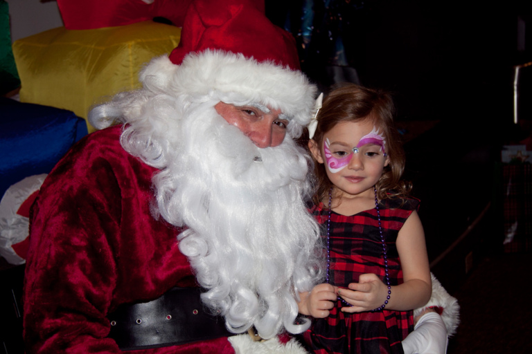 Young girl with pink face painting takes picture with Santa at the International Center for Limb Lengthening pediatric holiday party