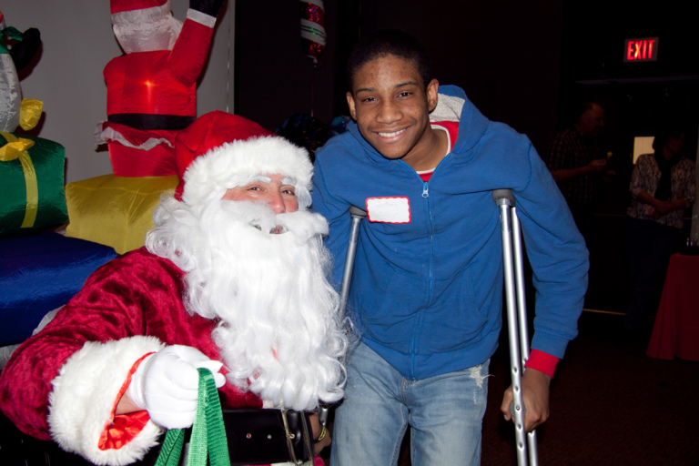 Boy with crutches smiles for a photo with Santa at the International Center for Limb Lengthening pediatric holiday party