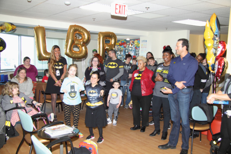 Patients of all ages, families and staff gather in the clinic waiting room with large gold L.B.R. balloons at the International Center for Limb Lengthening’s Leonard B. “Batman” Robinson Memorial Valentine’s Day Party