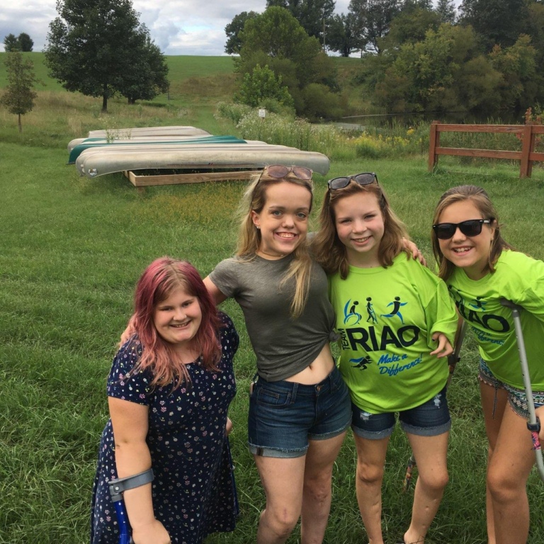 4 female patients, 1 with forearm crutches and 1 with crutches, pose for a picture together in a field during Rubin Institute for Advanced Orthopedics 2018 Save-A-Limb Pool Party event