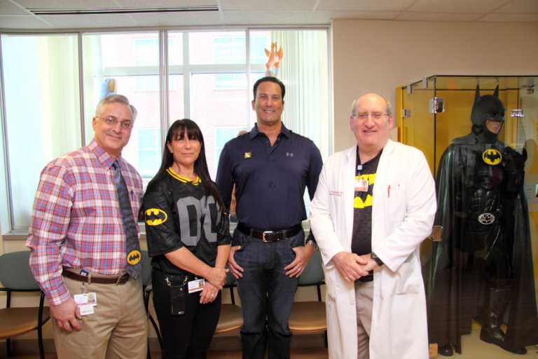 Dr. Shawn Standard and Dr. John Herzenberg pose with the family of Leonard B. “Batman” Robinson by glass case with Batman costume at the International Center for Limb Lengthening’s Leonard B. “Batman” Robinson Memorial Valentine’s Day Party