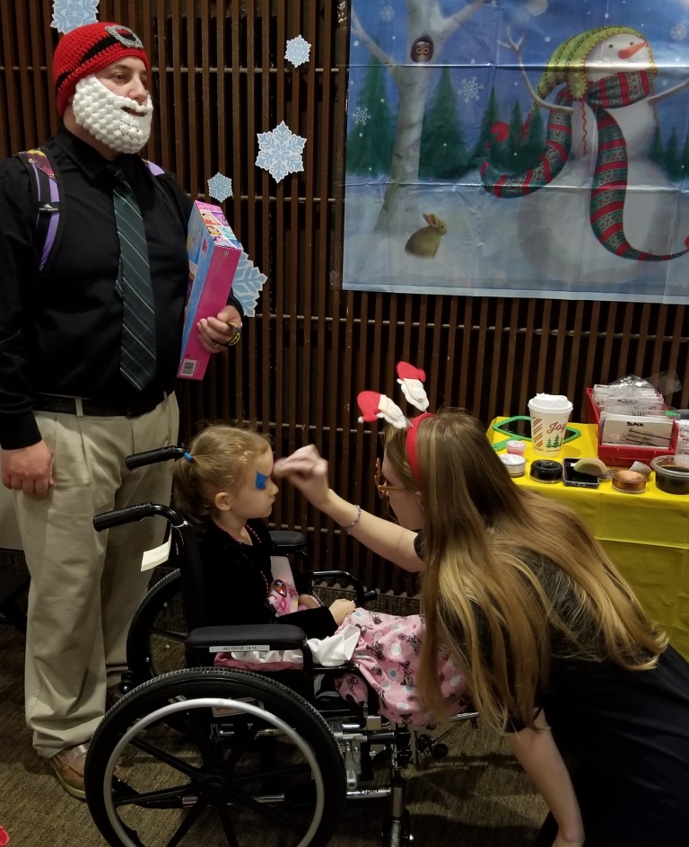 Young girl in wheelchair gets her face painted at the International Center for Limb Lengthening pediatric holiday party