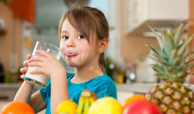 Child drinking milk with fresh fruit on table in kitchen