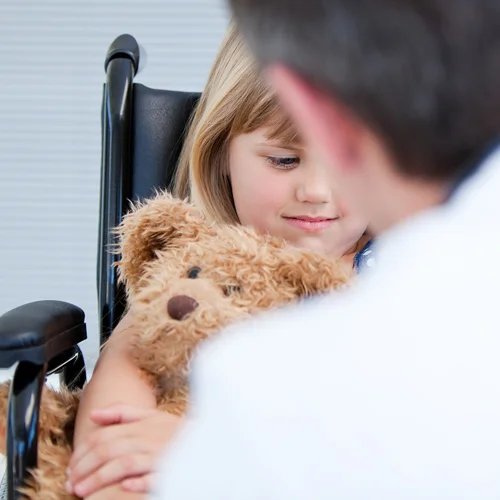 Doctor talking to a little girl in a wheelchair holding a teddy bear to help her manage her pain after surgery