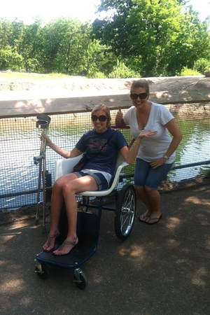 A female friend giving a thumbs up and Carly as a young woman in a wheelchair and holding forearm crutches during internal lengthening