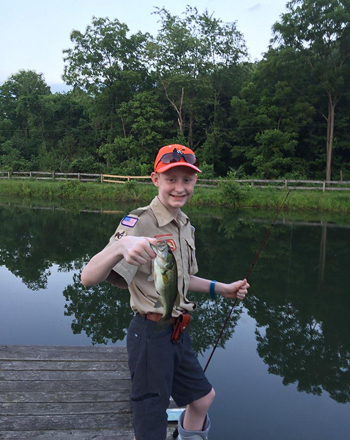 Gary holding up a fish he caught by a lake while wearing a walking boot