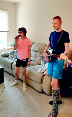 Gary in a leg cast playing electric guitar and his sister with a microphone playing a rock band video game 