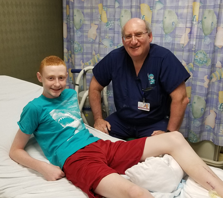 Gary reclining back with leg elevated in clinic bed next to Dr. John Herzenberg