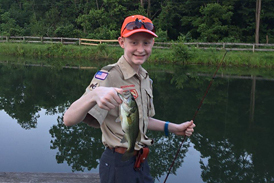 Gary holding up a fish he caught by a lake while wearing a walking boot