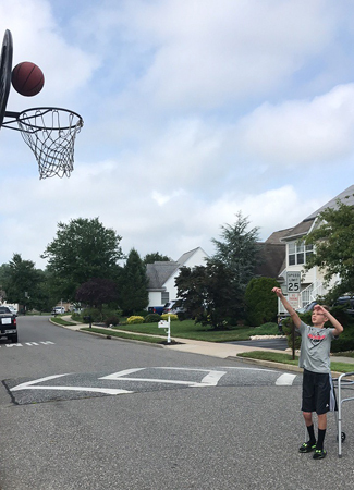 Jeffrey shooting a basket in a basketball hoop on the street with a walker behind him while being treated with a Precice internal nail and 8 plate