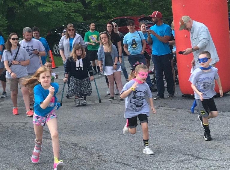 3 children—2 in super hero masks and capes-- racing out in front of the other walk participants