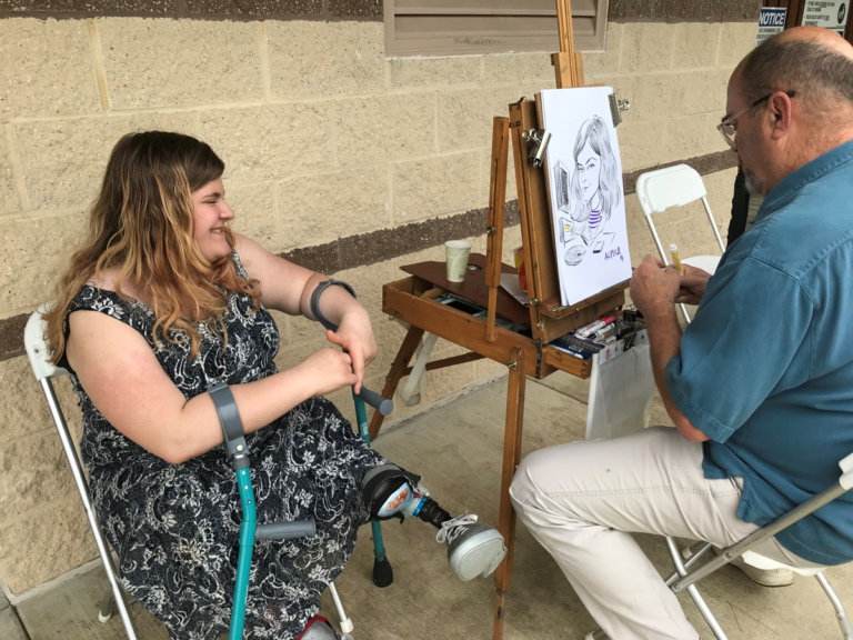 A young patient with crutches sitting while an artist draws her caricature