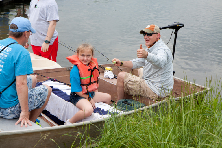 Dr. Shawn Standard giving a thumbs-up sign in a boat with a young girl patient in a life jacket and her father