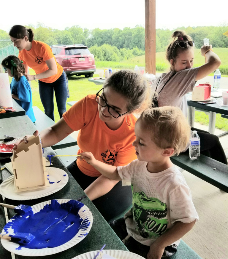 A volunteer assisting a very young boy patient painting a wood bird house