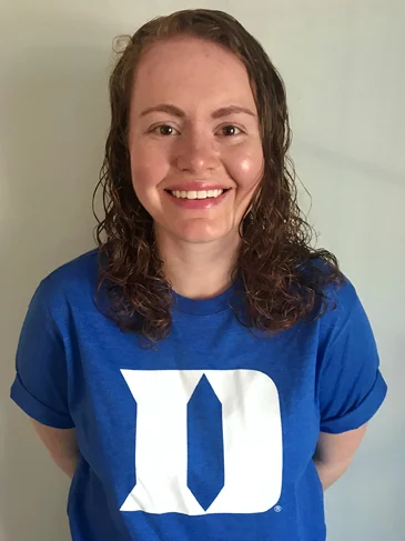 Carly proudly smiling in her Duke graduate school t-shirt