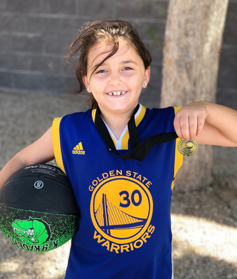 Gracie holding a basketball and a medal after she was cleared to play basketball again