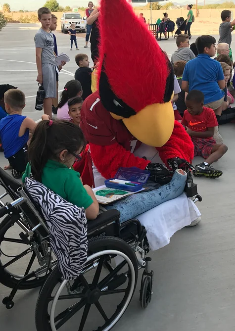 Gracie in a wheelchair with the Arizona Cardinals' mascot signing her cast
