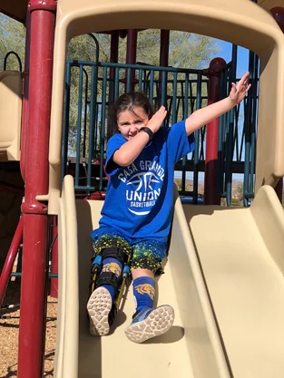Gracie wearing a leg brace on a playground sliding board