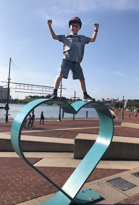 Jadon posing in a champion stance atop a large metal heart sculpture at Baltimore's Inner Harbor